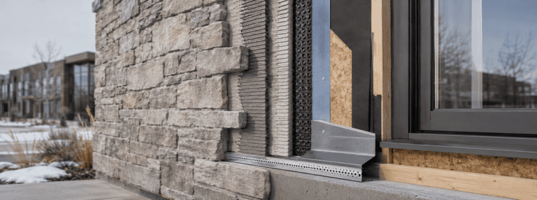 Cutaway exterior wall showing adhered stone veneer, mortar, drainage layer, flashing and window interface.